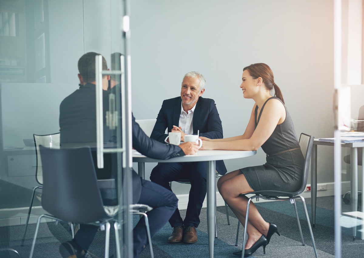 Three people in a meeting room. Open windows and two cups of coffee on the table.